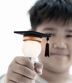 School boy holding up a light bulb with graduation hat