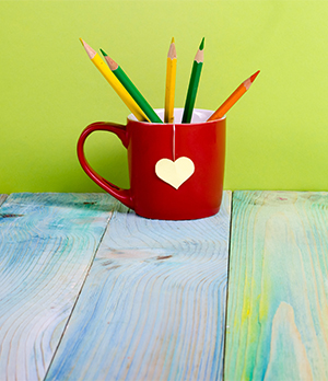 Red coffee mug with heart filled with colored pencils